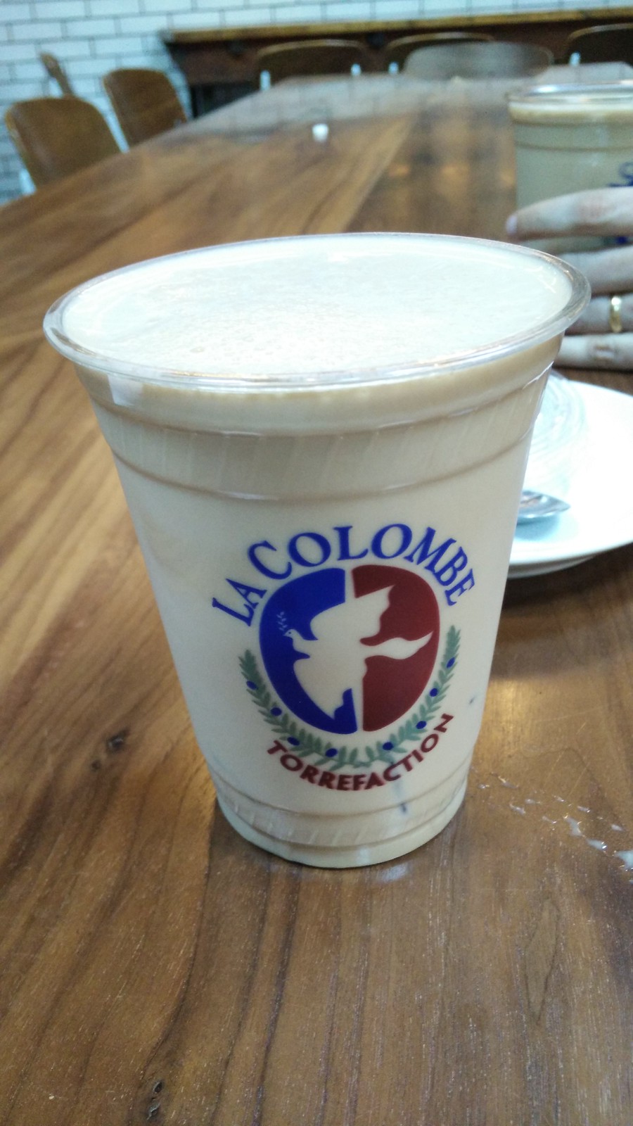 木のテーブルに置いた La Colombe のカップ入りドラフト・ラテ、細かい泡