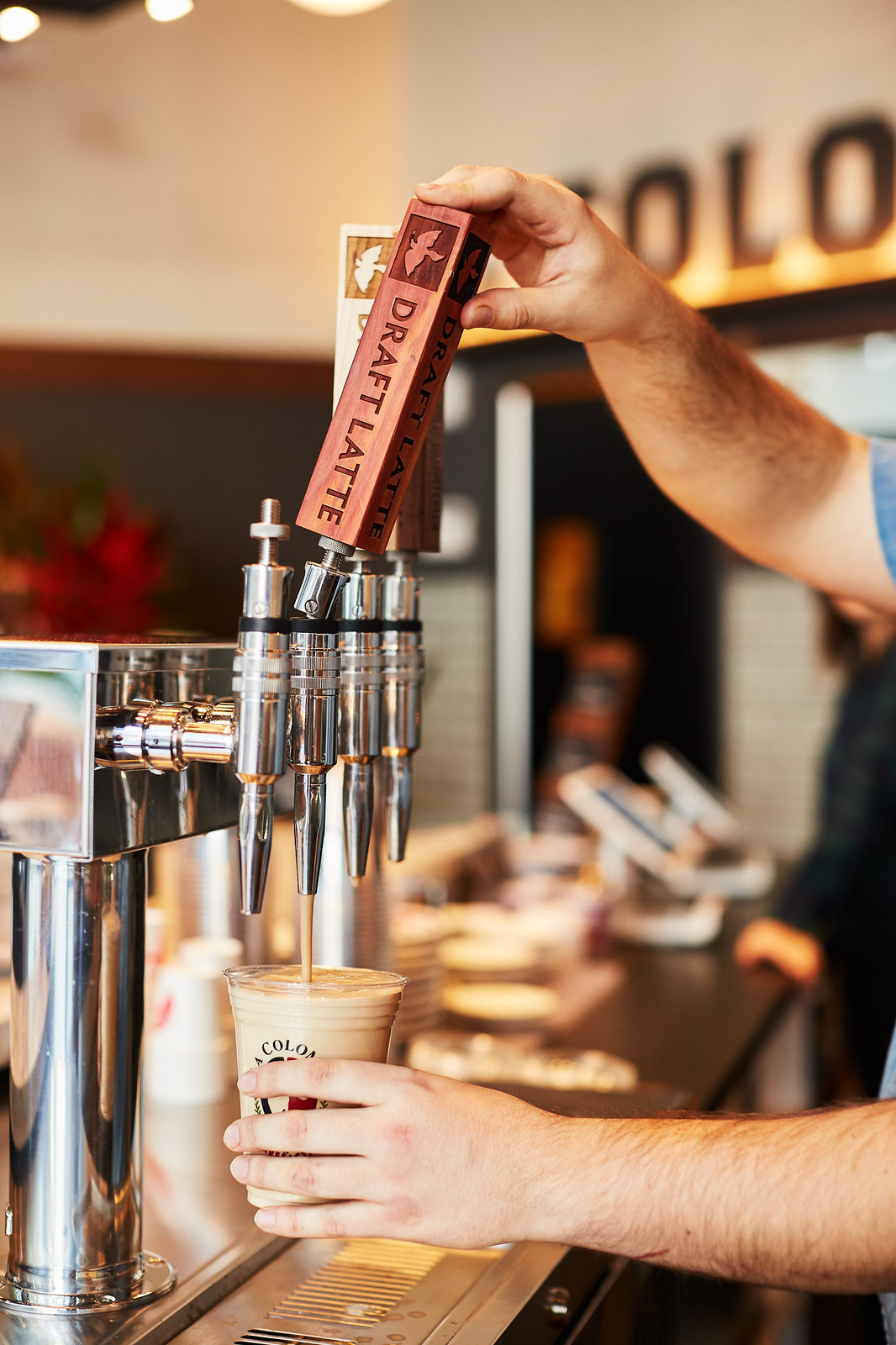 DRAFT LATTE と書かれたタップのハンドルを引き、カップに注ぐところ