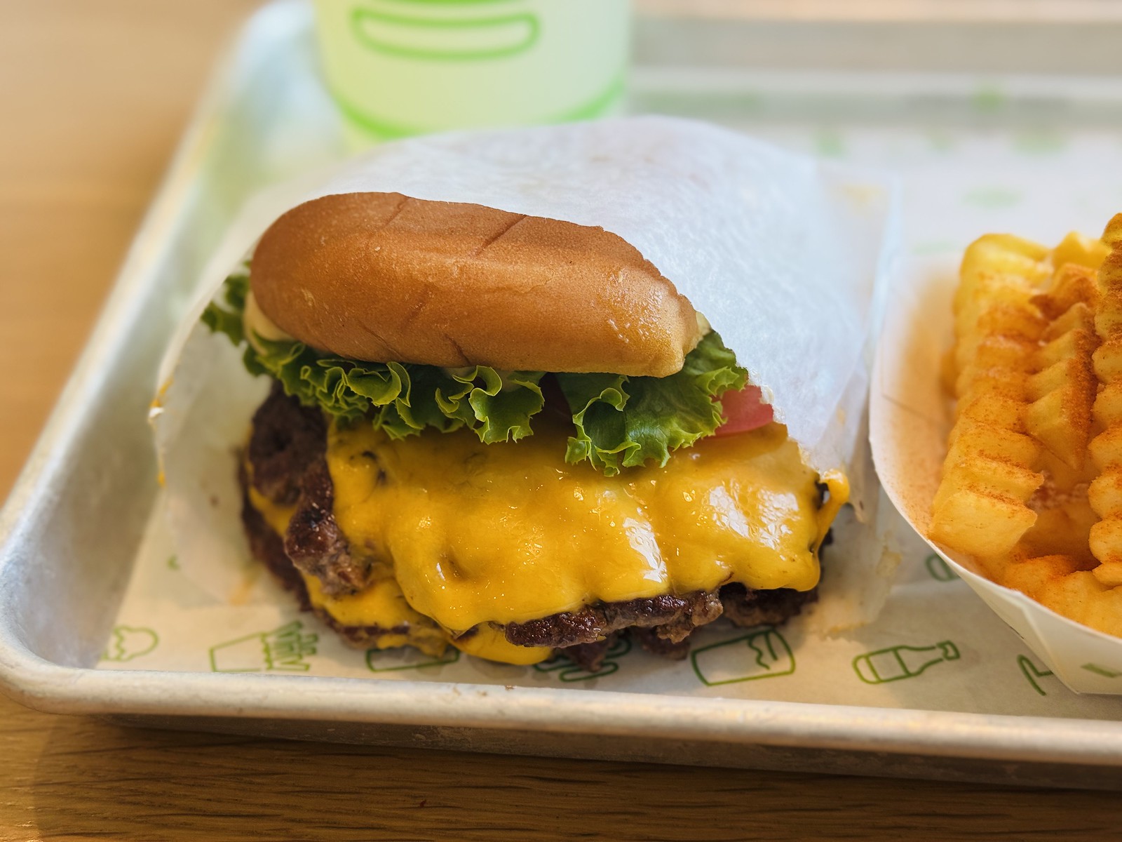 トレーの紙包みに入ったシャックバーガー、とろけたチーズとレタス・トマト、クリンクルカットのフライ