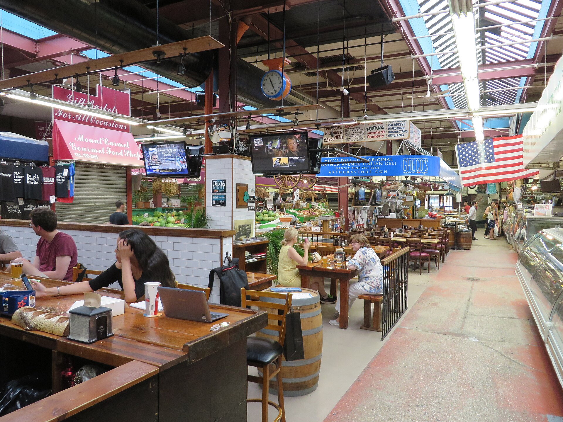 Arthur Avenue Retail Market の中、屋台と木の卓が並ぶ