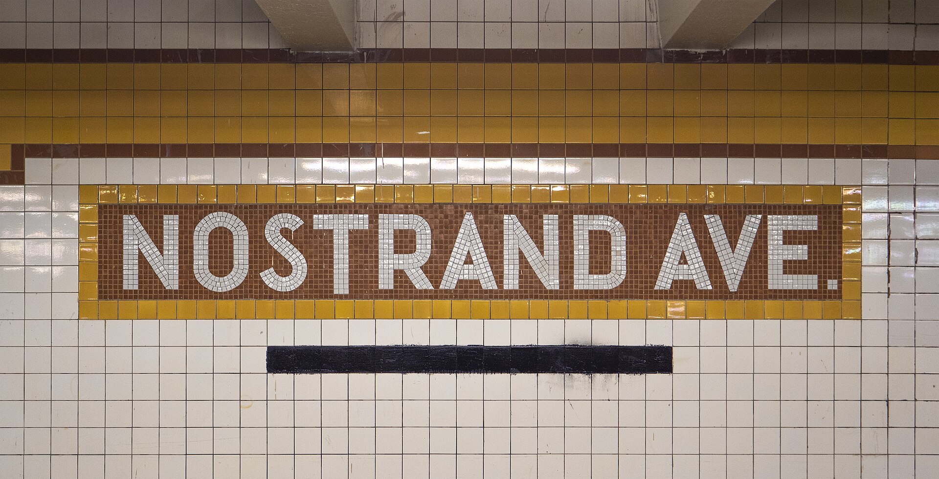 白いタイル壁に NOSTRAND AVE. と書かれた地下鉄駅の駅名モザイク