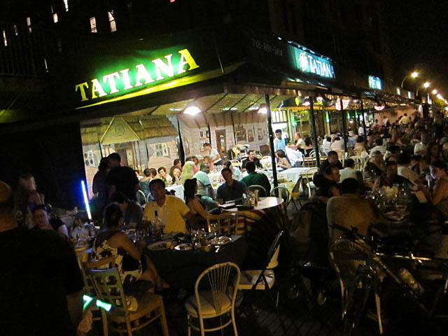 夜の Tatiana の看板と、ボードウォーク沿いのテラス席を埋める客
