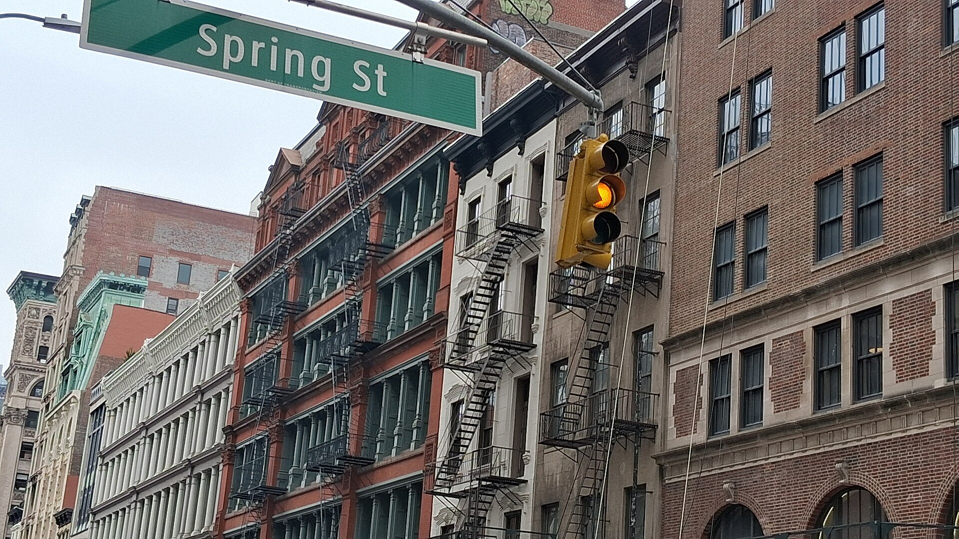 Spring St の道路標識と信号、赤れんがと鋳鉄の建物が並ぶソーホーの通り