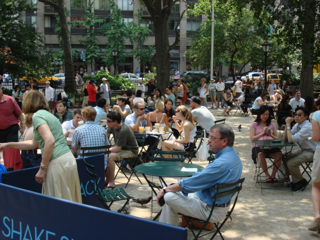 公園の木陰のテーブル席でバーガーを食べる人々、SHAKE SHACK の囲い