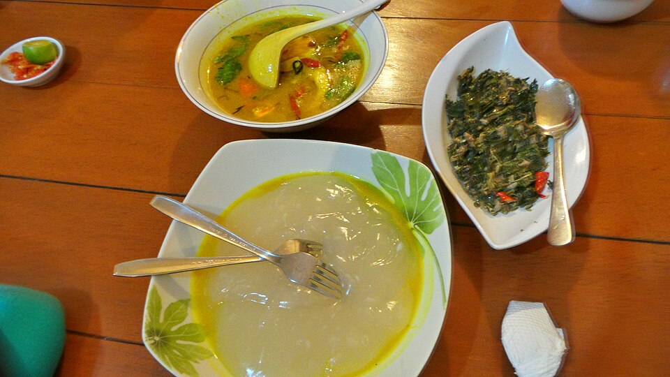 皿に広げた半透明のパペダと、黄色い魚のスープ、キャッサバの葉とパパイヤの花を混ぜた青菜のおかず