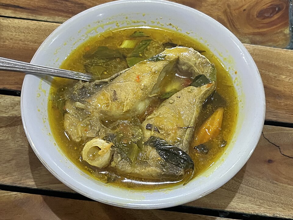 白い深皿に盛られた、ターメリックで黄色く染まった魚のスープ。魚の切り身と青菜が入っている