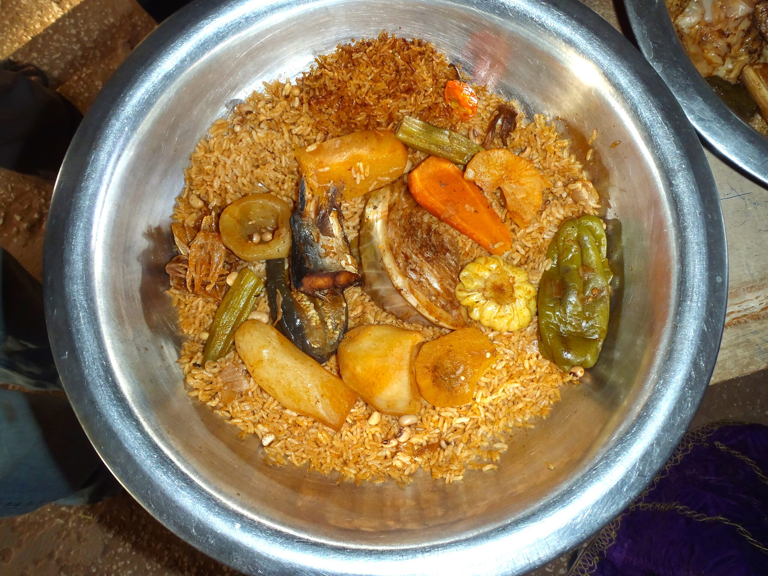 大皿に盛ったチェブジェン（赤い炊き込みご飯、魚、キャッサバ、にんじん、ピーマン）