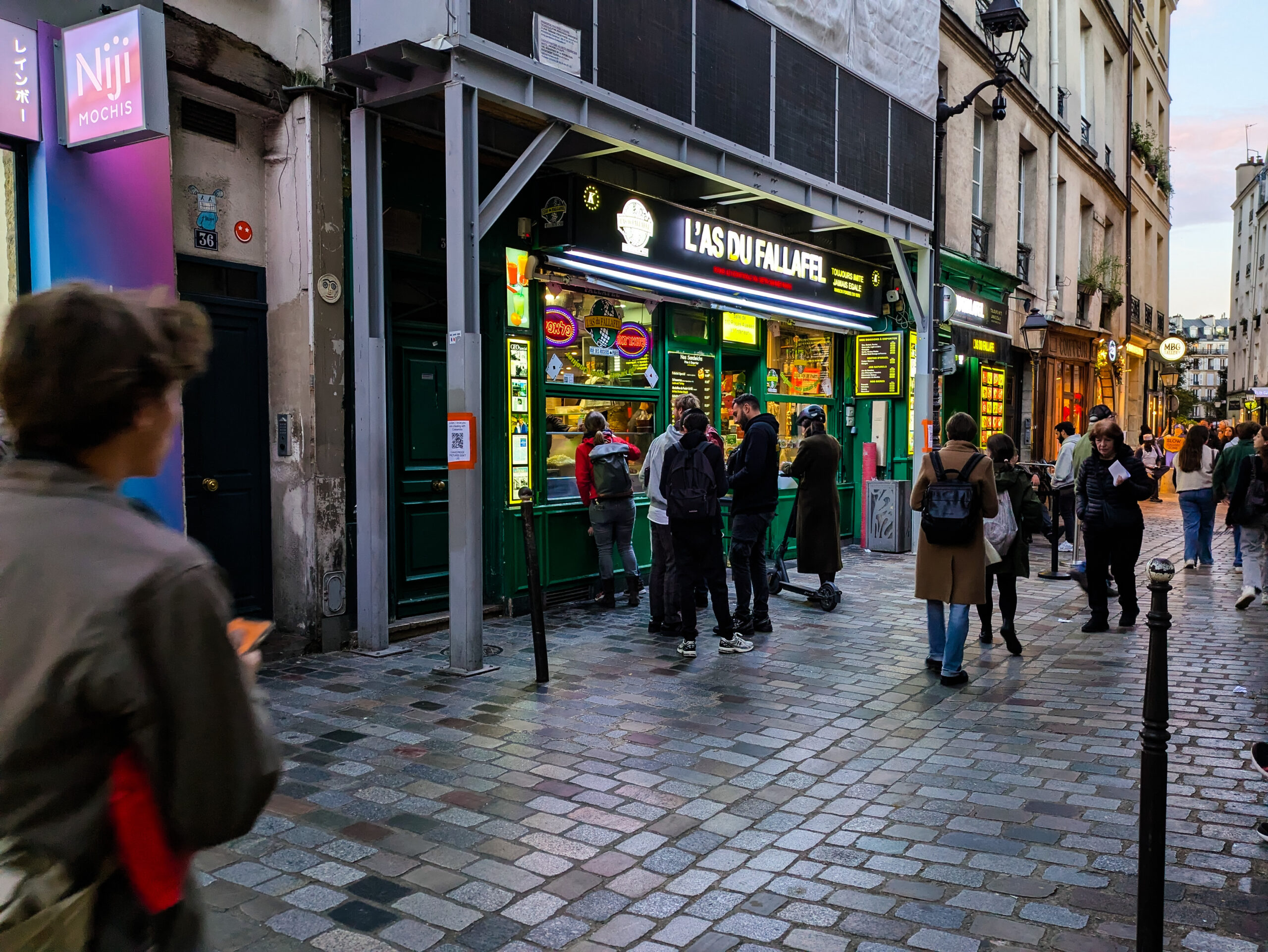 ロジエ通りの石畳とファラフェル店の店先、通行人