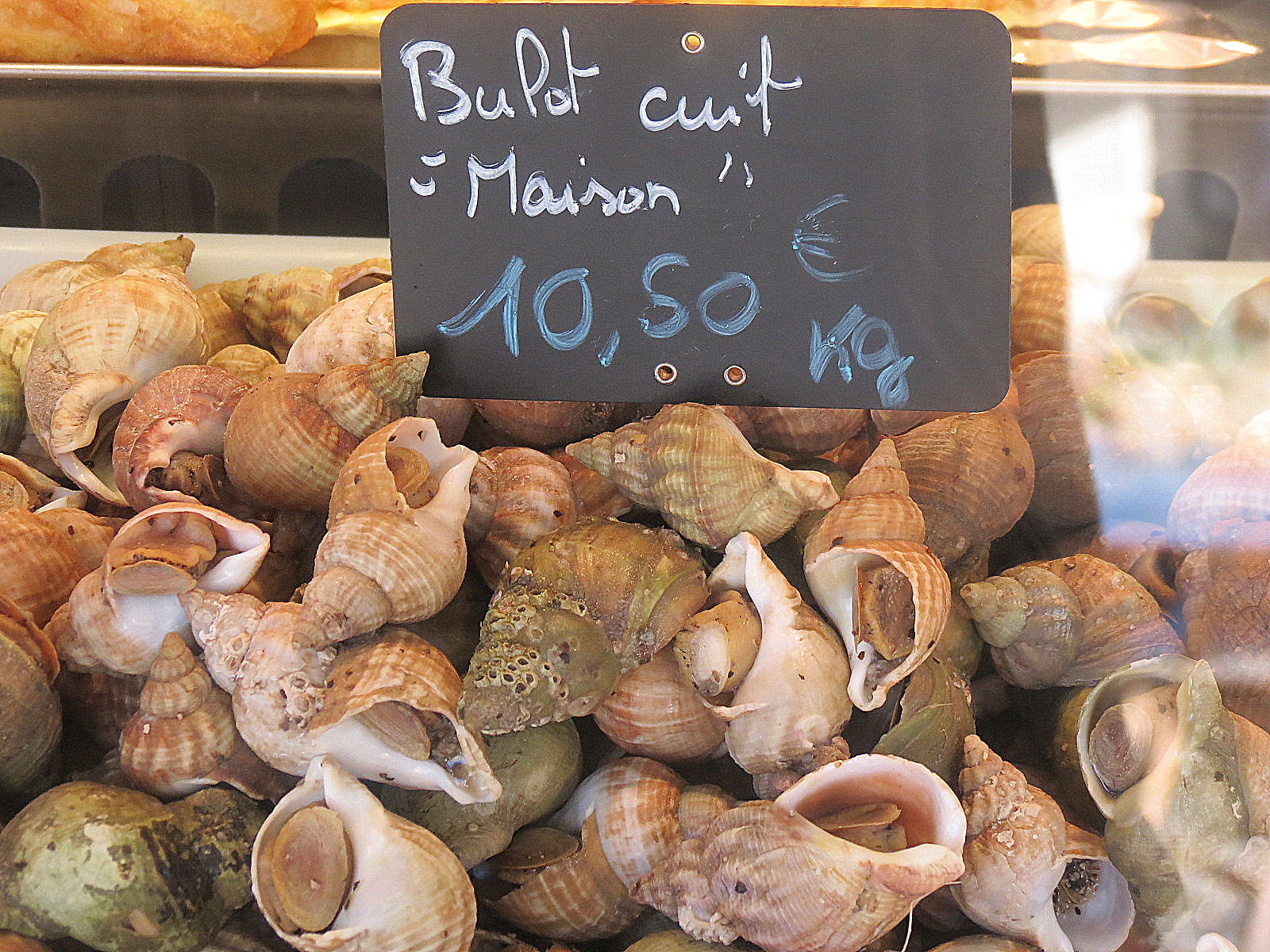 魚屋の台に積まれたゆでツブ貝と「Bulot cuit maison」の値札