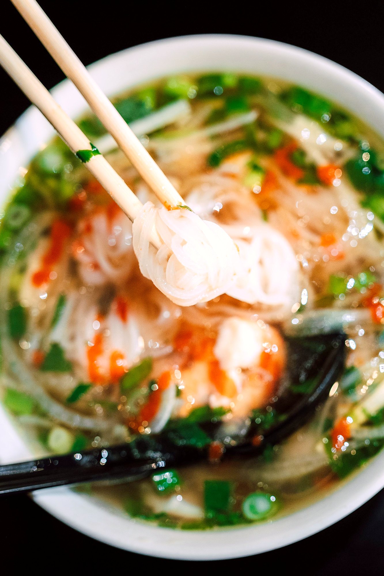 箸で持ち上げられた白く平たい米の麺