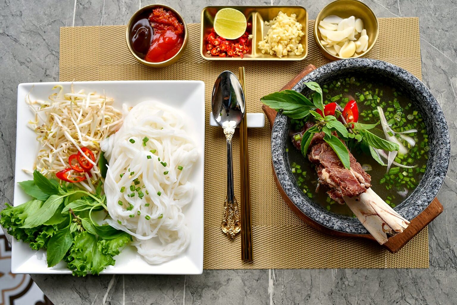 卓の上に、麺の器、スープの丼、香草ともやしの皿、たれの小鉢が並んでいる