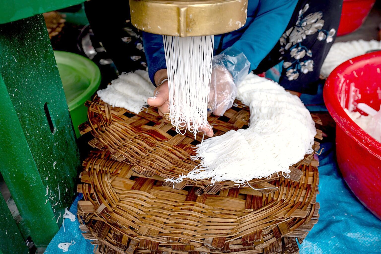 ベトナムの市場で、手で米の麺をかごに押し出してまとめている人
