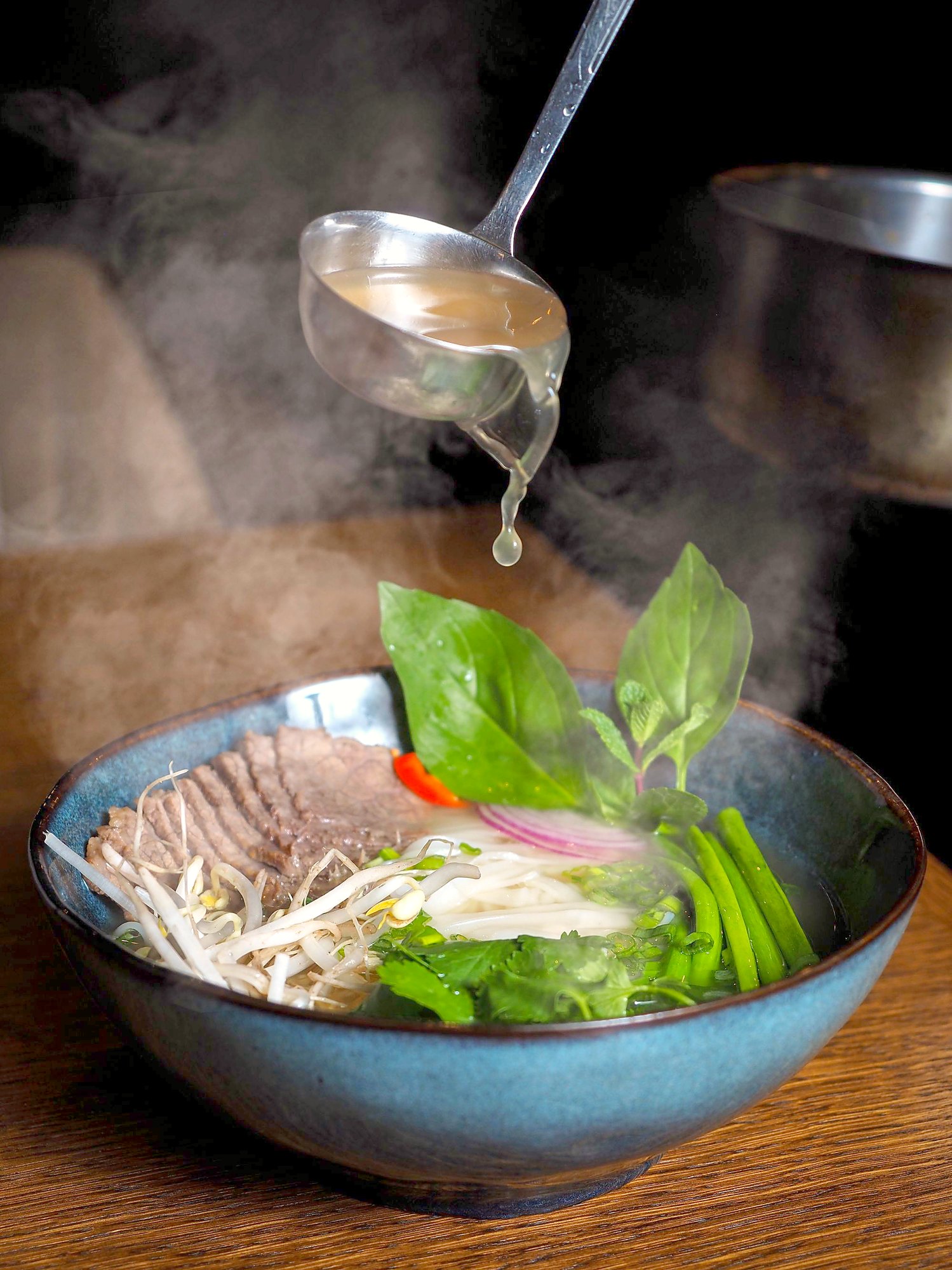 湯気が立ちのぼる麺のスープ。バジルと薄切りの玉ねぎがのっている