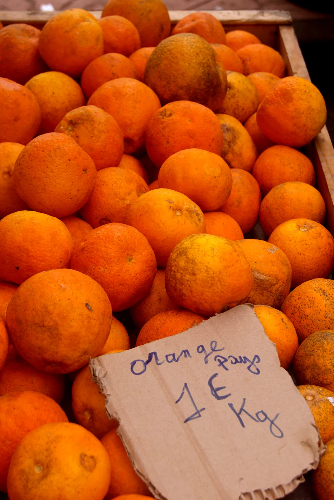 「oranges pays 1€ kg」の札を立てたオレンジの山